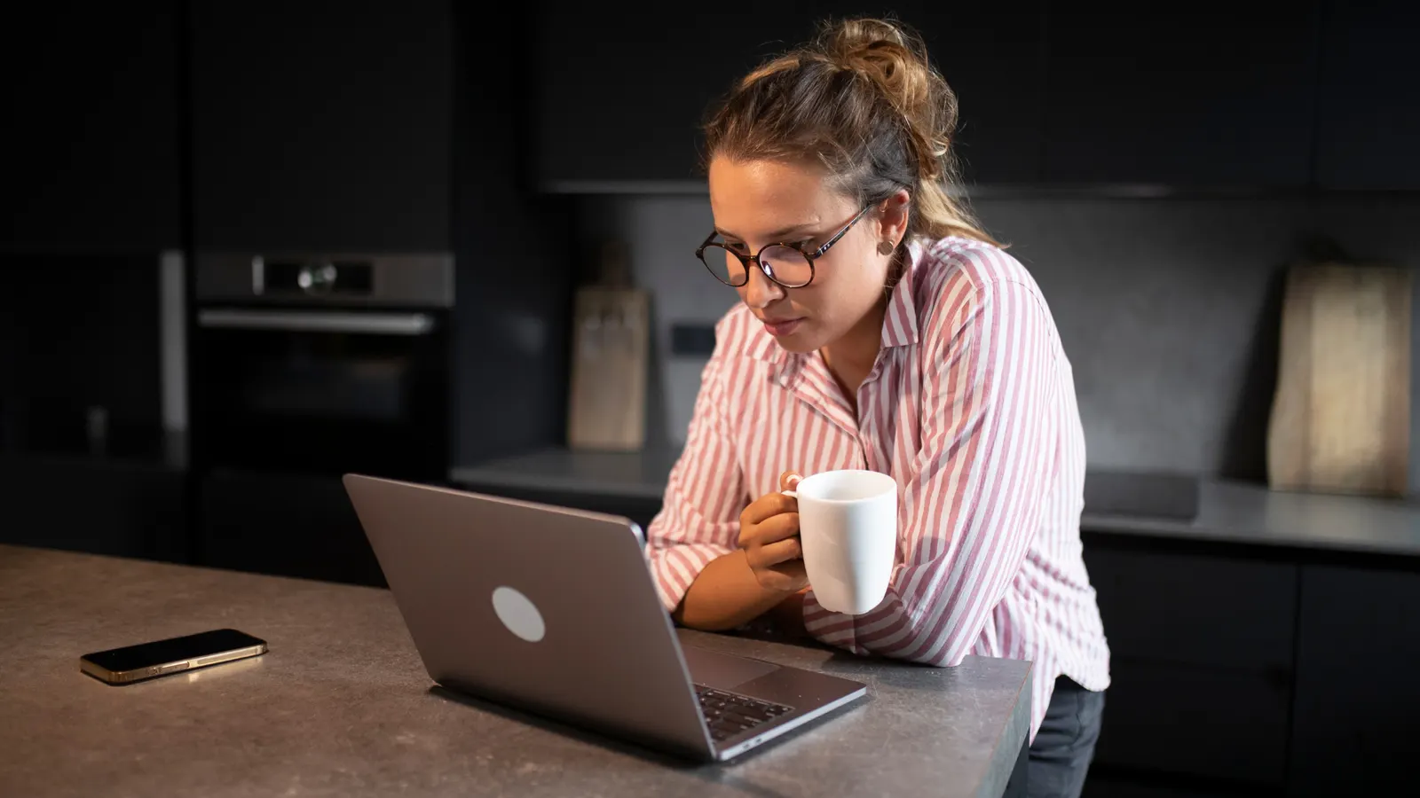 A person working at a laptop, holding a mug.