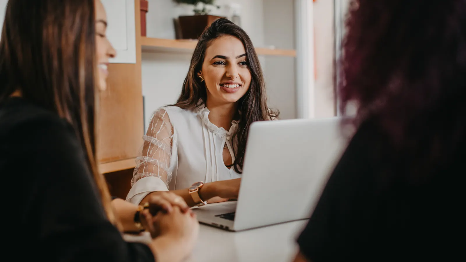 A colleague smiling while working together at a laptop with a colleague in the foreground.