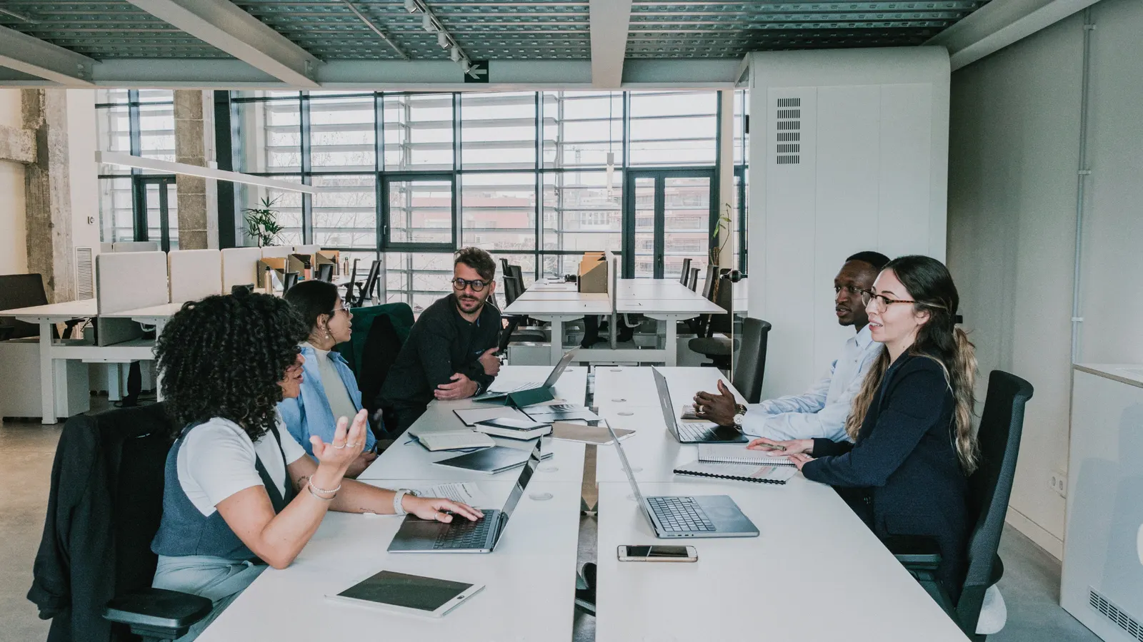 Colleagues in discussion around a table in a bright, modern open-plan office.