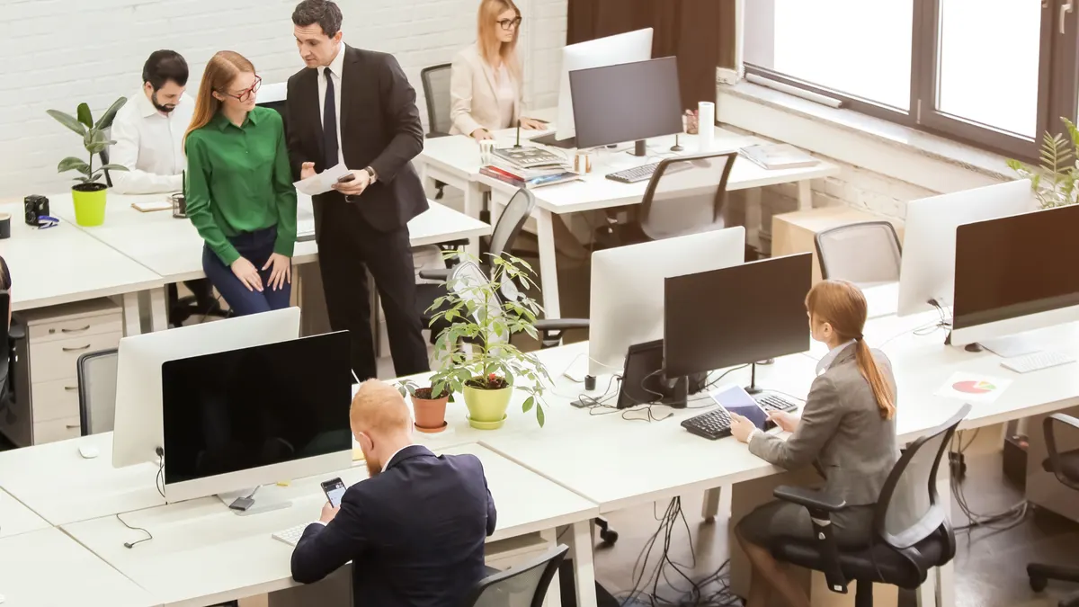 Colleagues working at desks in a busy, modern open-plan office.