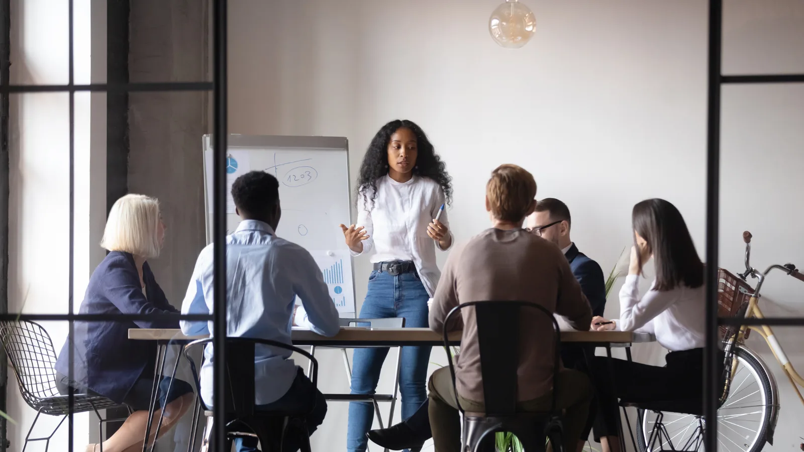 A colleague presenting ideas at a whiteboard covered in notes and charts to a small team gathered around a table.